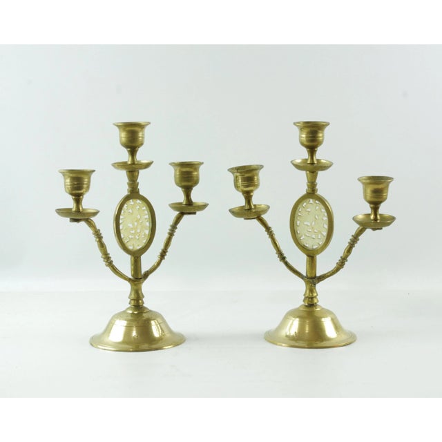 A set of two vintage brass candelabra, each with three candle holders and a carved jade inset in the center. The oval jade...