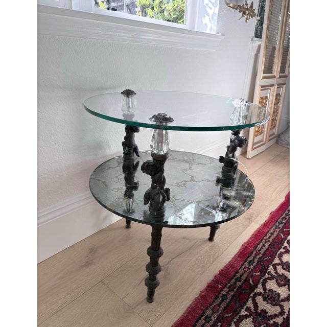 Elegant vintage Hollywood Regency style side table featuring sculptural cherub supports, decorative faceted glass accents,...
