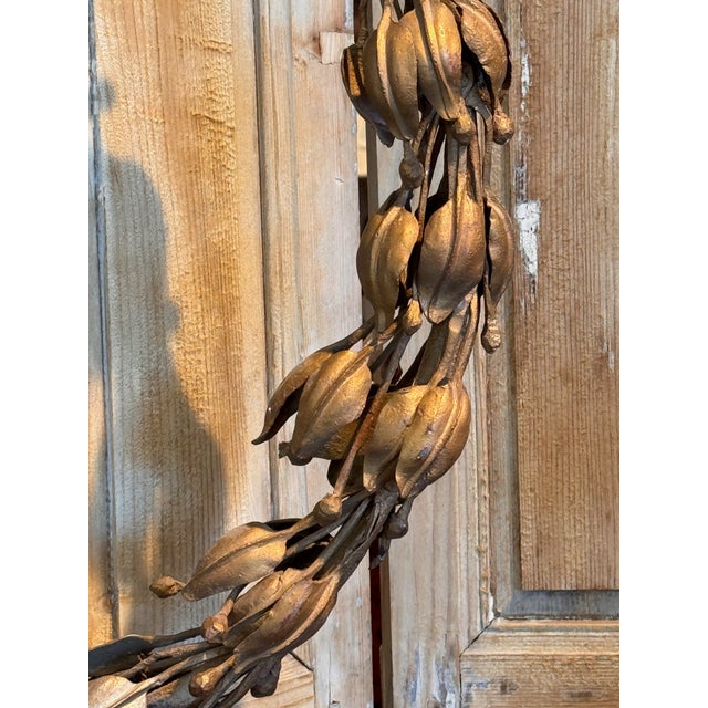 Gilt tole wreath formed as an oval garland of seed pods and buds on slender stems, gathered at the top beneath a tied...