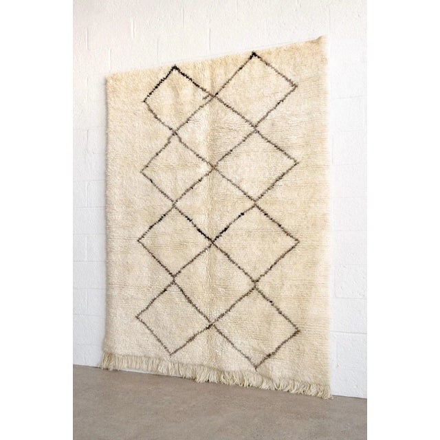 This vintage handwoven Moroccan Berber Beni Ourain area rug features a simple deep charcoal and brown line diamond lattice...