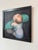 The painting depicts a vulnerable figure, a baby clad in a diaper and green flotation devices, gazing upward with an...