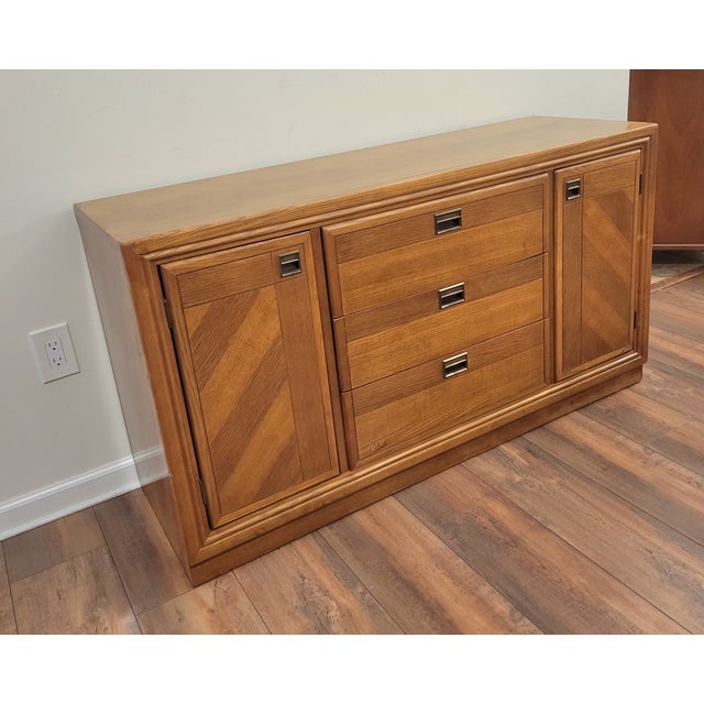 This 1960s Mid-Century Modern oak sideboard and credenza by Bernhardt Furniture features distinctive diagonal parquet door...