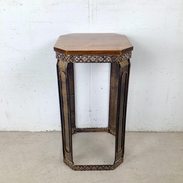 This decorative pedestal table features a tall, architectural silhouette topped with an octagonal wood surface. The warm...