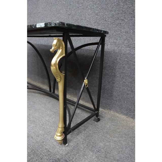Maison Charles style console table featuring a black steel frame, brass seahorse-form supports, and a rectangular verdi...