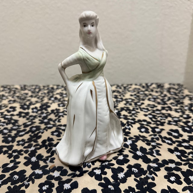 This elegant vintage porcelain figurine depicts a woman in a graceful pose. She is dressed in a long white gown with a and...