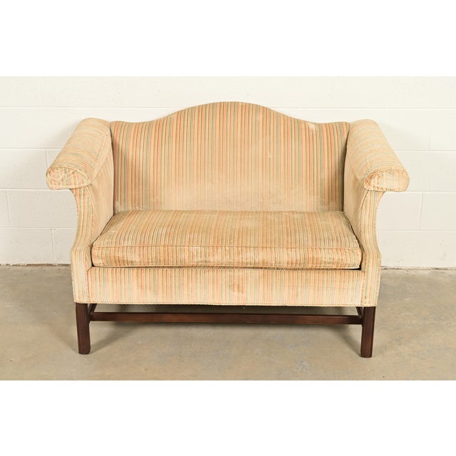 A gorgeous Chippendale style camelback upholstered loveseat or sofa with carved mahogany legs and stretchers By Ethan...