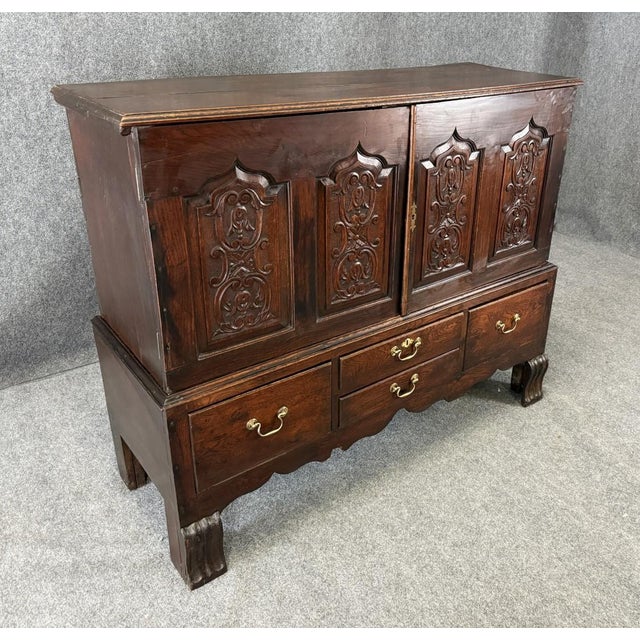 This 18th Century carved oak chest on stand features cathedral-style paneled doors with intricate floral and scrollwork...