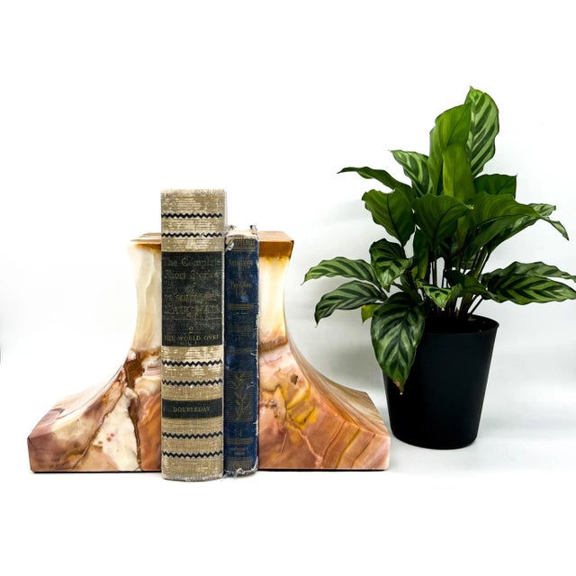 Striking pair of vintage sculpted onyx bookends featuring swirls of pink, cream, amber, and honey-toned veining. The...