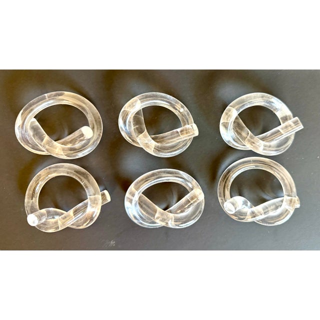 This fun and sculptural set of six vintage lucite napkin rings, likely made circa 1970s-1980s, feature a playful pretzel...
