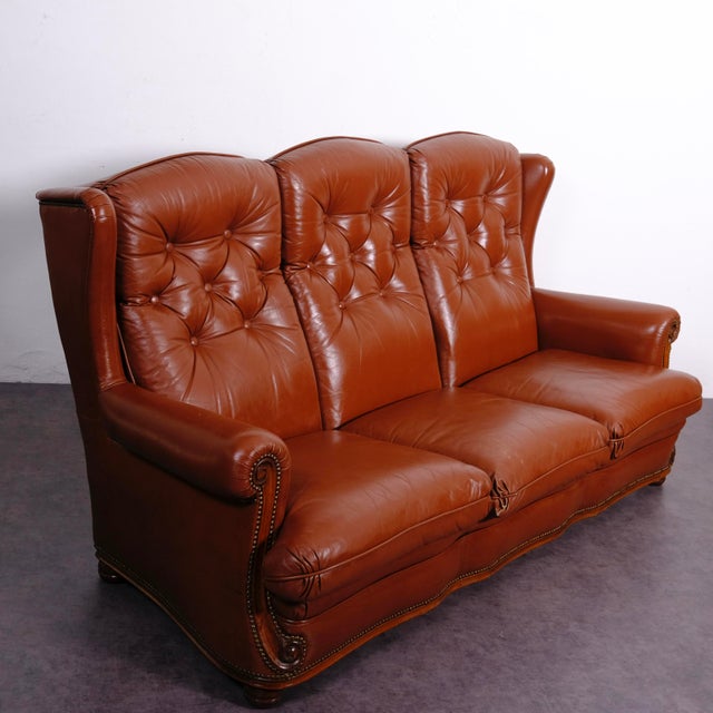 Beautiful brown Chesterfield-style sofa features distinctive button-tufting on the three high-back cushions. The seat...