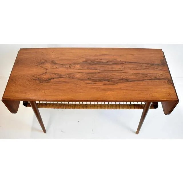 Mid-century modern coffee table features woven rattan lower shelf and 8" drop leaves on each end. It measures 21-1/2" tall...