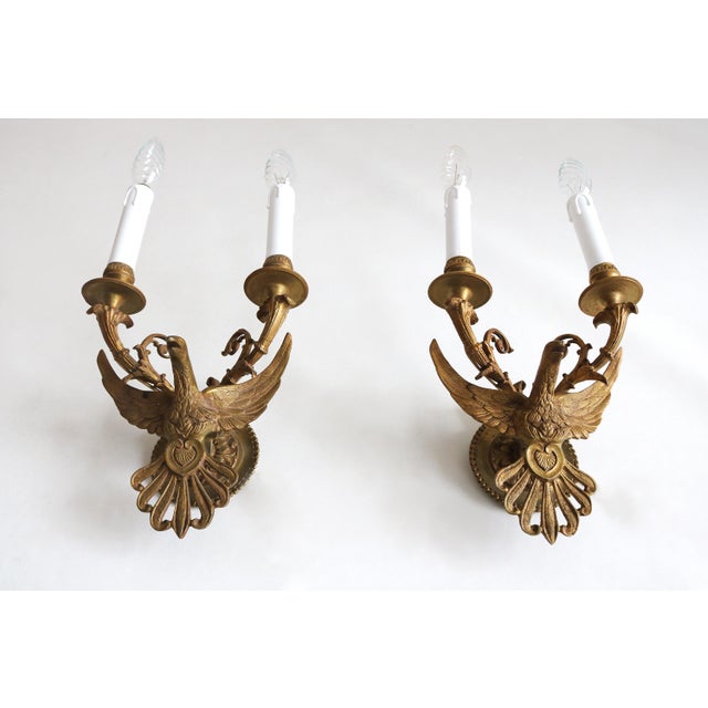 Beautiful pair of antique brass wall sconces with detailed eagle motifs and outstretched wings. The elegant scroll arms...