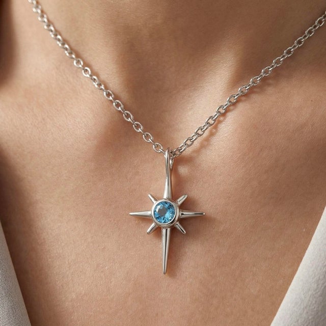 Elegant and celestial in design, this refined pendant showcases a brilliant Blue Topaz gemstone at the center of a sleek...