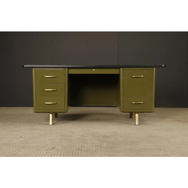 A classic American mid-century modern steel tanker desk, circa 1960s, featuring a olive green finish and custom protective...