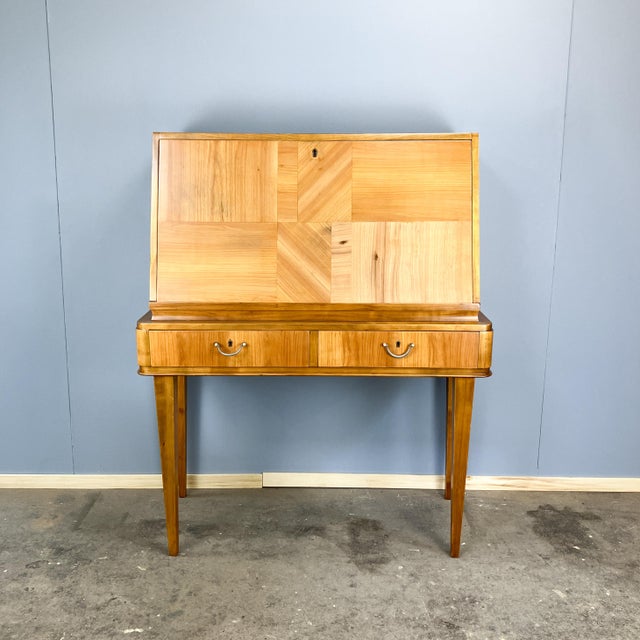 A delicate secretary desk from the 1940s with a strikingly clean design and a beautiful, geometric front. Behind the drop-...