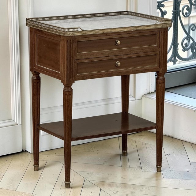 A finely crafted French Louis XVI style end table in solid mahogany, crowned with beautifully veined Carrara marble and...