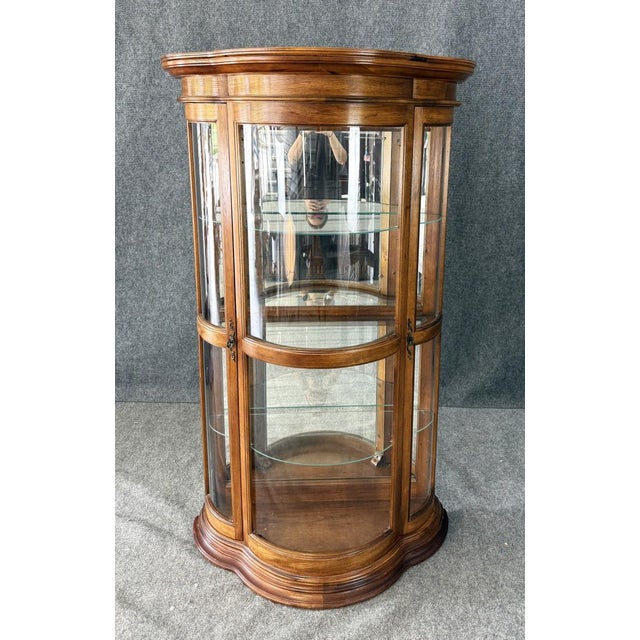 This Pulaski Furniture Co. bombe front curio cabinet features a gracefully curved silhouette with wraparound glass panels,...