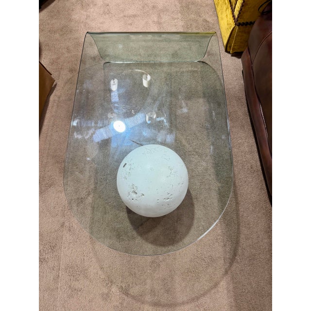 Striking postmodern waterfall coffee table featuring a sleek, curved glass top paired with a sculptural plaster orb base....