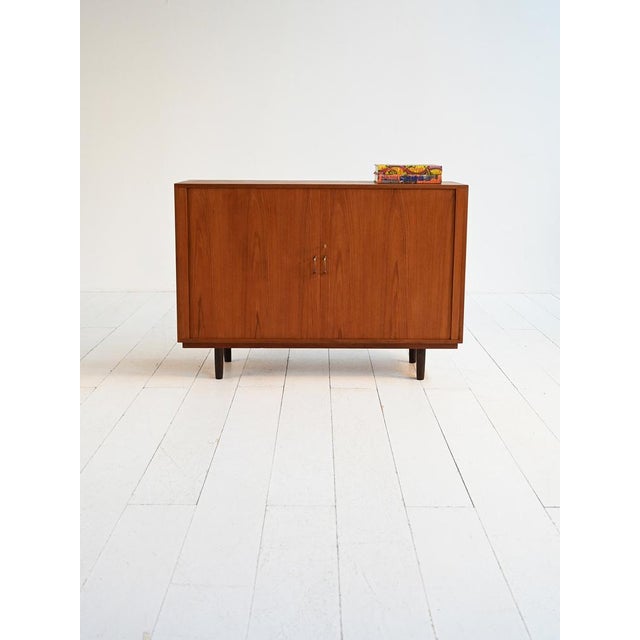 Teak cabinet with roll-up doors, internal pull-out trays, and brass details. Scandinavian production, 1950s. Scandinavian...