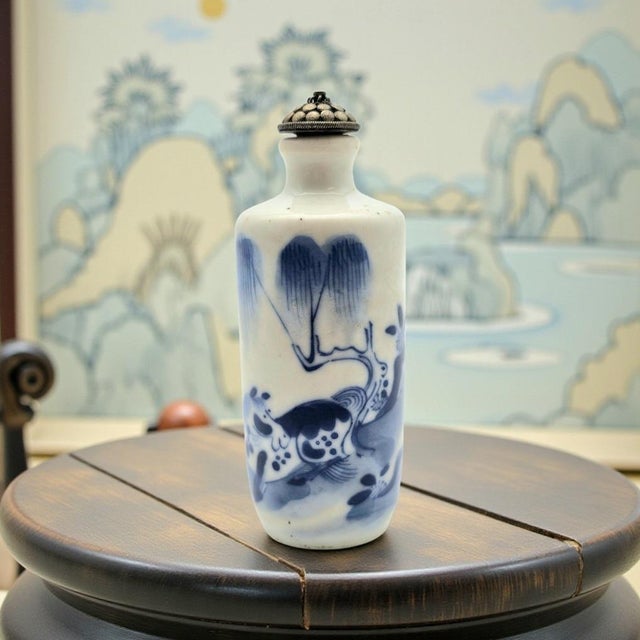 This Chinese porcelain snuff bottle is decorated in underglaze cobalt blue, featuring a stylized landscape composition...
