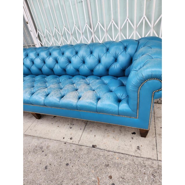 Tufted leather sofa in a vibrant blue color. This Chesterfield style piece has deep button tufting across the back, seat,...