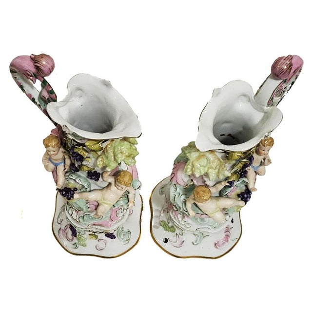 A very unique pair of antique porcelain pitchers with children & grape vines surrounding the piece. I have not been able...