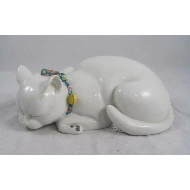 An exceptional and highly expressive Japanese porcelain figure of a sleeping recumbent cat in white ground and wearing a...