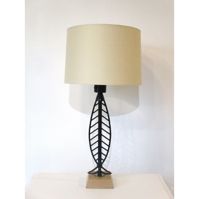 A welded iron satin black bodied table lamp with a fish bone motif sitting on a wooden base with brass detail . Topped...