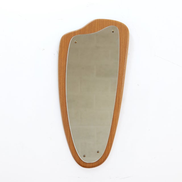 This mid-century wall mounted mirror was made in England during the 1960s. The mirror has an asymmetrical shape and would...