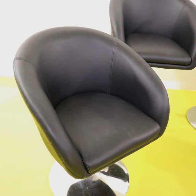 Set of four black faux leather swivel armchairs with chrome base.