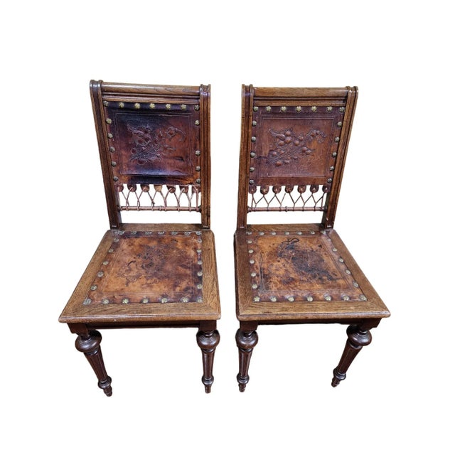 Unique striking pair of early 1900s French embossed leather hall chairs. Construction looks to be of oak and walnut....