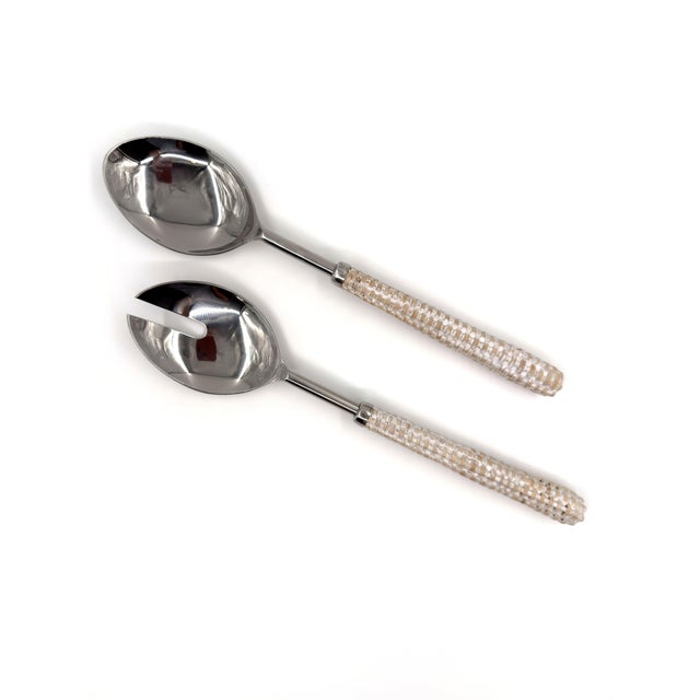 A refined set of handmade salad servers featuring polished stainless steel heads and handwoven rattan-wrapped handles....
