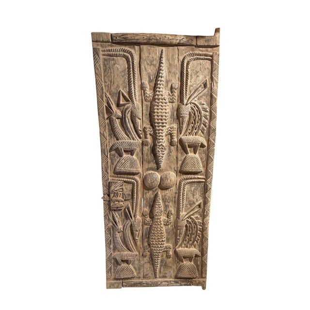 This vintage Dogon granary door from Mali showcases exceptional carved relief artistry, featuring four standing chiwaras...