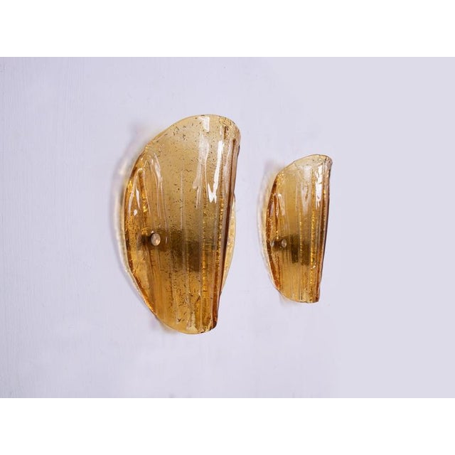 Elegant set of two mid-century wall lights made of heavy, thick, amber murano glass mounted on a brass frame. Gem from the...