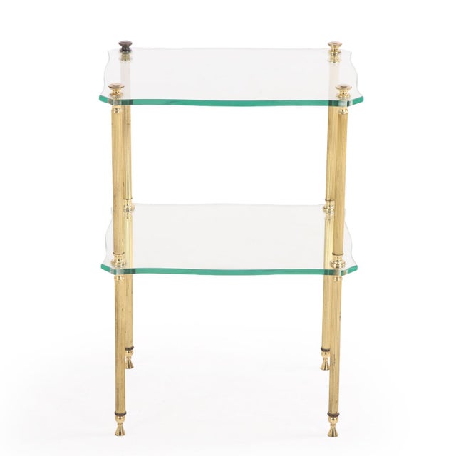 Featuring a sleek brass plated iron cylindrical legs supporting two tiers of shaped glass shelving. Dating to circa 1960,...