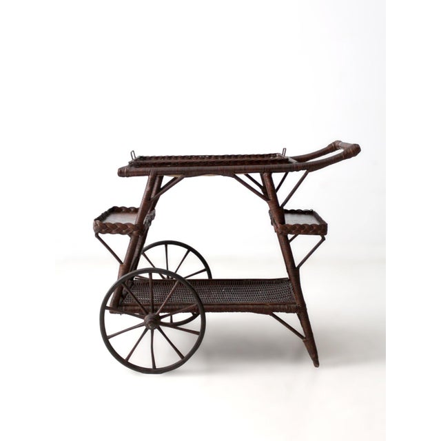 An early 1900s American wicker bar cart featuring a balanced silhouette and a tiered trolley form. The piece includes...
