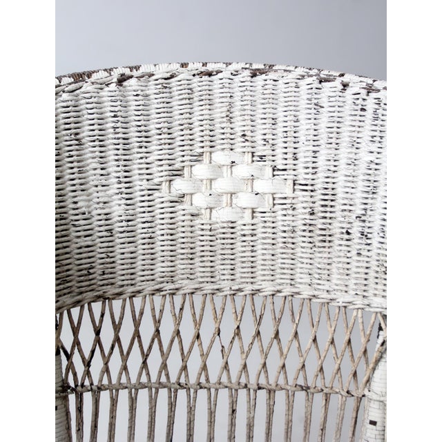 An antique American wicker rocking chair featuring a rounded barrel back, open lattice sides, and softly flared arms set...