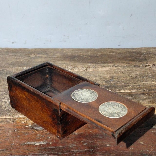 This vintage Chinese rosewood storage box features two inset decorative Qing dynasty silver dollar coins on the front...