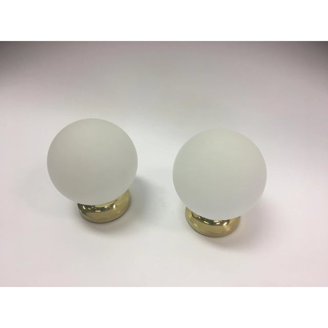 This pair of similar table lights comprise opaline glass orbs on a brass base. I have official proof of authenticity such...