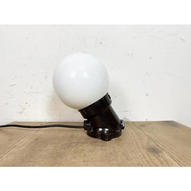 Vintage industrial light made in former Czechoslovakia the 1970s. It features a brown bakelite wall mounting and a milk...