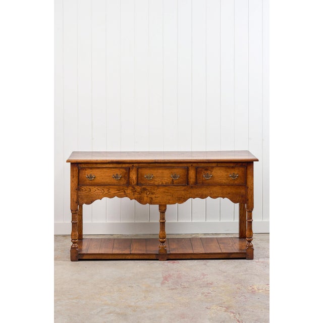 This 19th century English oak dresser base/console features three drawers with traditional brass bail pulls set above a...