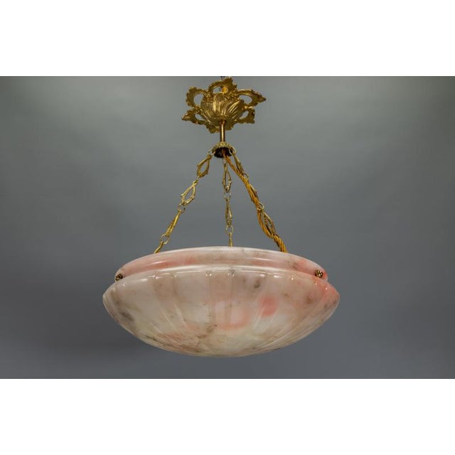 Rare pink-toned french art deco alabaster pendant with sculptural bowl form and elegant bronze detailing. A rare and...