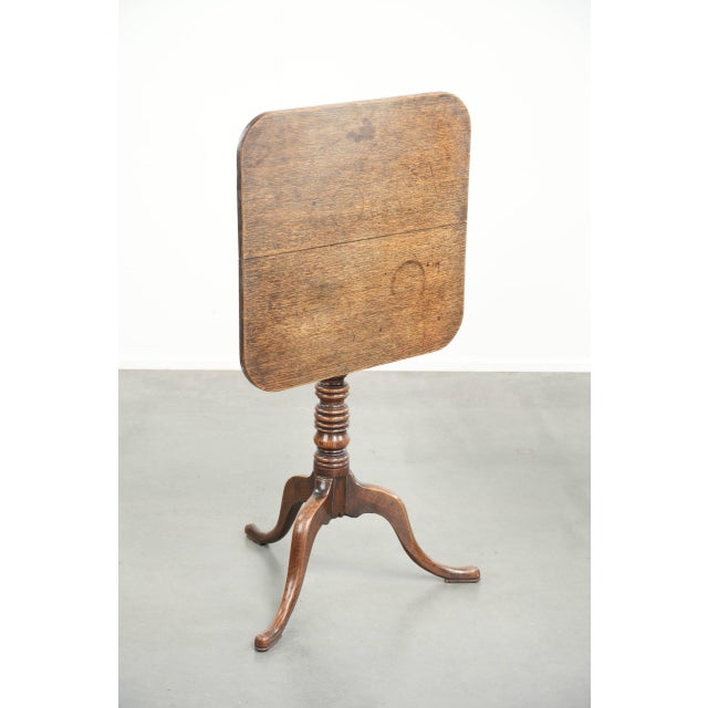 This antique English oak tilt-top table/side table has a unique square shape and dates from the early 19th century. The...