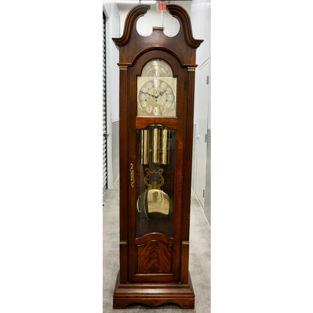 This is a vintage cherry wood grandfather clock featuring a swan-neck pediment, a brass dial with a moving moon phase...