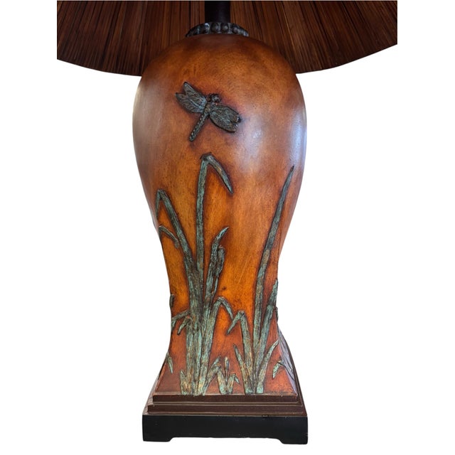 A richly detailed accent lamp with a warm amber-brown body, raised reed and cattail motifs, and a sculptural dragonfly...