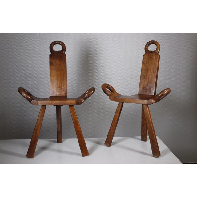 Pair of mid century brutalist tripod side chairs in light tinted wood, with hand carved details on the handles. Both are...