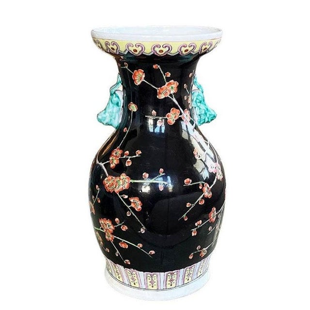 A tall famille noire chinoiserie vase with a red and green floral motif throughout the body on a black background....