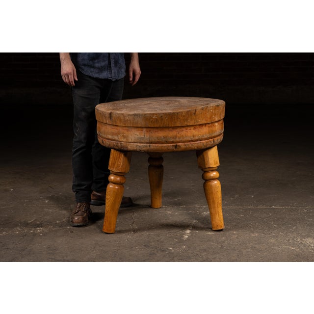 A solid round butcher block table with hand-turned legs and a thick end-grain maple top. The surface shows concentric...