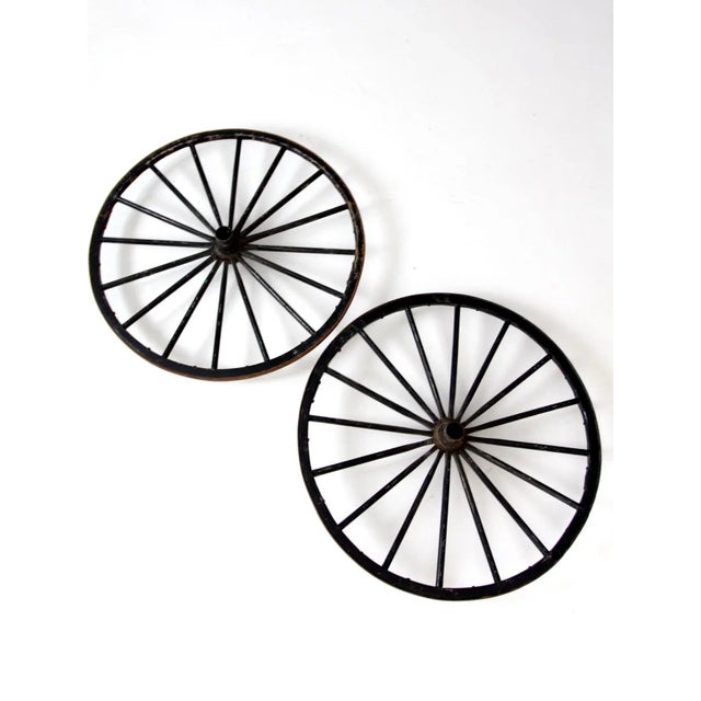 This pair of antique wooden wagon wheels features decorative black painted spokes paired with metal hubs, bearings, and...