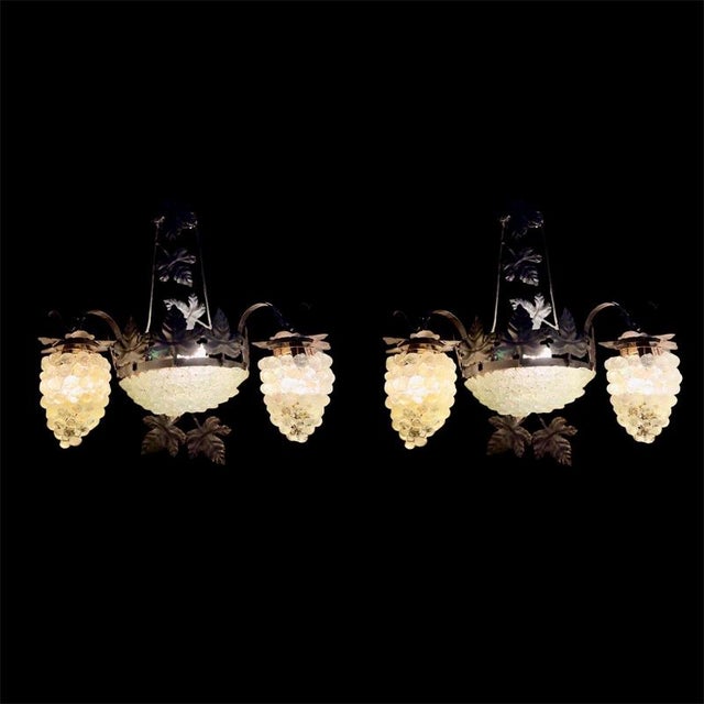 A striking pair of two-arm wall sconces in dark wrought iron, adorned with hand-cut vine leaves and pendant clusters of...
